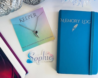 May include: A blue journal with the text "MEMORY LOG" and a silver feather design. A silver necklace with a lightning bolt charm on a card that says "KEEPER" and "Never underestimate the power of the page". A blue and white sticker with the name "Sophie" on it.