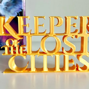 May include: A gold-colored 3D printed sign that reads "Keeper of the Lost Cities".