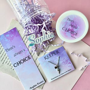 May include: A gift set with a clear jar filled with purple paper shreds, a bookmark, a small round container, a name tag, and a necklace. The bookmark and container have the text "There's always a CHOICE". The necklace card says "KEEPER".