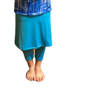 Può includere: Una camicia a maniche lunghe blu e bianca con un motivo geometrico e una gonna turchese. La gonna ha un pannello anteriore più lungo e un pannello posteriore più corto.