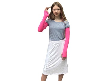 Puede incluir: Una mujer con una camiseta gris y una falda blanca con calentadores de brazos rosas. Lleva zapatillas blancas.
