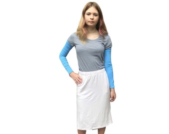 Puede incluir: Una mujer con una camiseta gris de manga larga con mangas azul claro, una falda blanca y zapatillas blancas. El atuendo es sencillo e informal, adecuado para el uso diario.