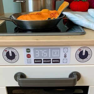 May include: A white toy stove with a black and silver burner, a digital display showing 375, and knobs labeled "HI", "OFF", and "LO". The stove has a gray handle and a white oven door.