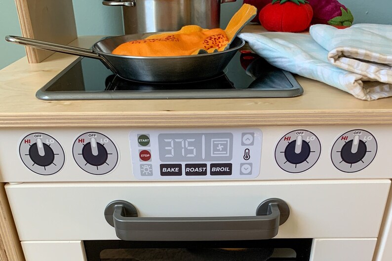 May include: A white toy stove with a black and silver burner, a digital display showing 375, and knobs labeled "HI", "OFF", and "LO". The stove has a gray handle and a white oven door.