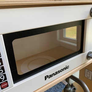 May include: White toy microwave with a black frame and a clear glass door. The microwave has a black Panasonic logo and a digital display with buttons labeled "Stop" and numbers 0-9.