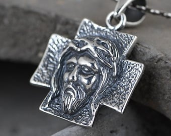 May include: A silver pendant necklace featuring a detailed cross with a sculpted image of Jesus Christ's face. The cross is textured and has a worn look.
