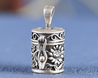 May include: A silver charm in the shape of a small, ornate box with a hinged lid. The box is decorated with floral designs and has a small loop at the top for attaching to a necklace or bracelet.