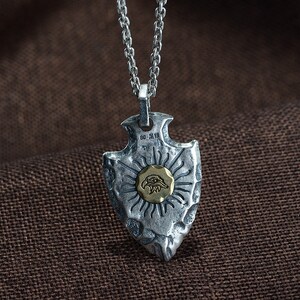 May include: Silver arrowhead pendant necklace with a gold eagle design. The pendant has a textured surface and a chain link necklace.