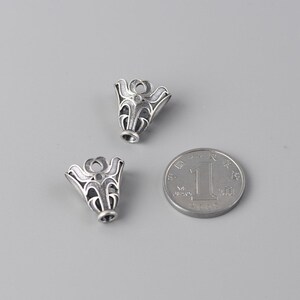 May include: Two silver-toned metal pendant caps with an intricate floral design. The caps are approximately the size of a Chinese yuan coin.