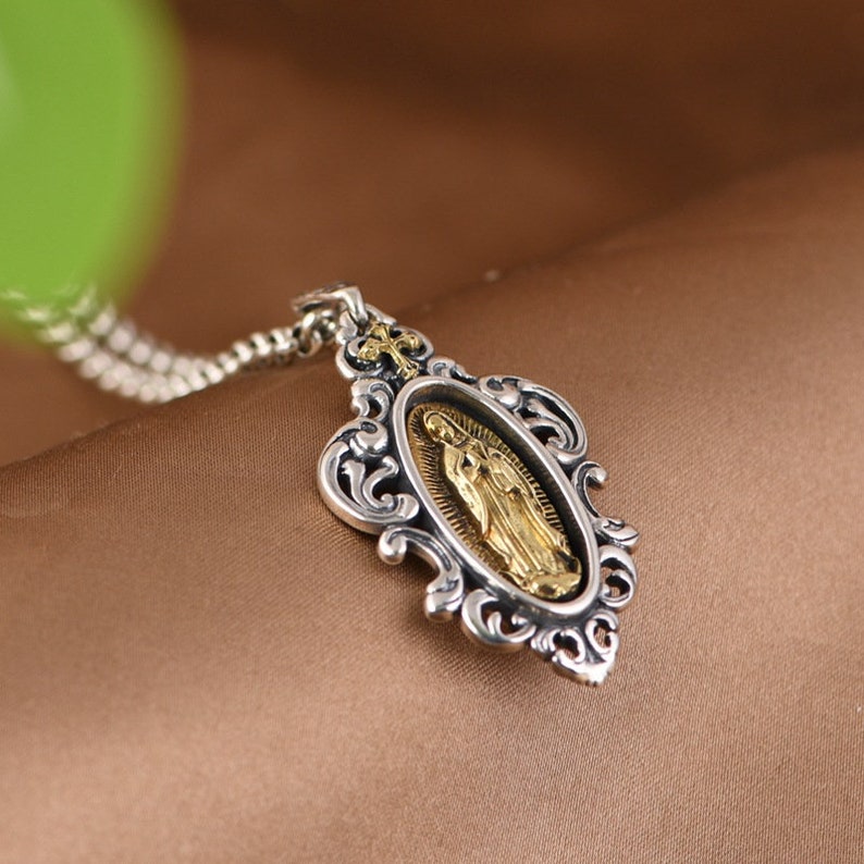 May include: Silver chain necklace with a silver and gold pendant featuring an ornate frame and a depiction of the Virgin Mary.