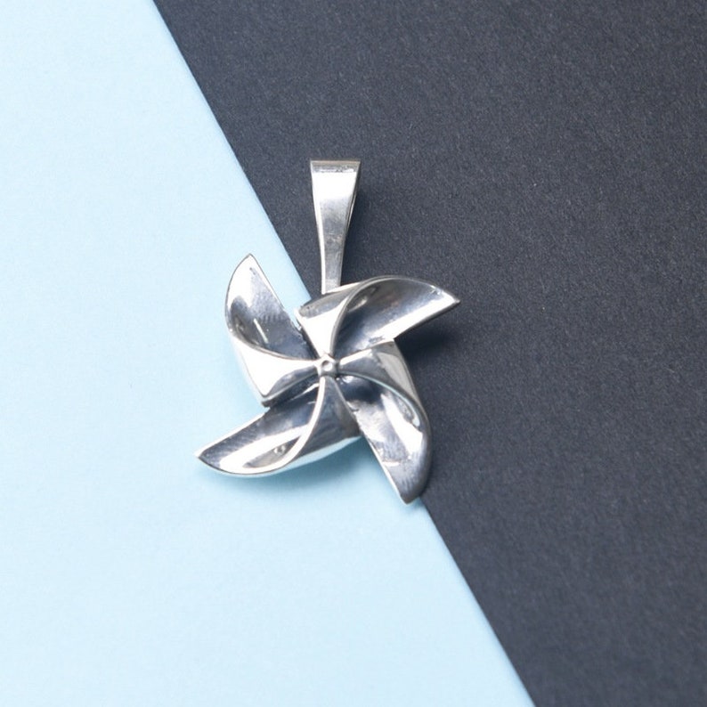 K&ouml;nnte beinhalten: Ein silberner Windm&uuml;hlen-Anh&auml;nger mit detailliertem Design. Die Windm&uuml;hle ist ein beliebtes Symbol f&uuml;r Kindheit und Verspieltheit.