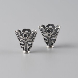 May include: Two silver, ornate, decorative, cone-shaped, metal caps with a floral design.