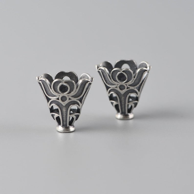 May include: Two silver, ornate, decorative, cone-shaped, metal caps with a floral design.