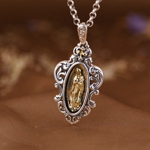 May include: Silver pendant necklace with a gold-toned oval medallion featuring a religious figure. The pendant has an ornate, filigree design.