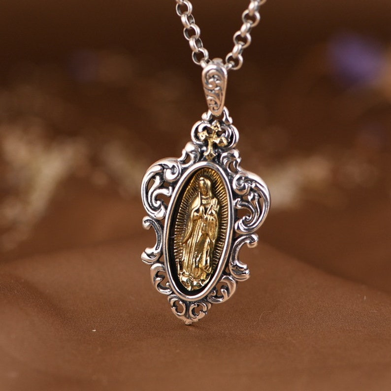 May include: Silver pendant necklace with a gold-toned oval medallion featuring a religious figure. The pendant has an ornate, filigree design.