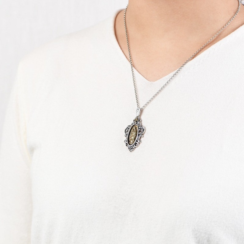 May include: A silver chain necklace with a gold oval pendant featuring an ornate design. The pendant has a detailed filigree frame.