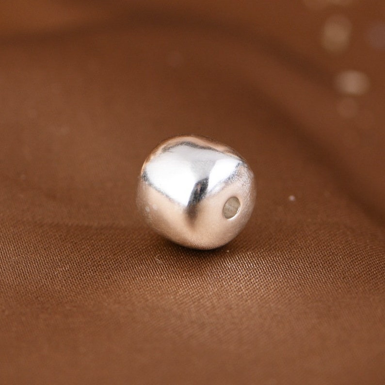 Peut inclure: Une perle argent&eacute;e de forme ronde et lisse avec un petit trou au centre.