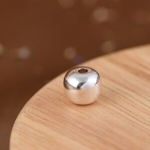 Peut inclure: Une perle ronde en argent avec un trou au centre. La perle est lisse et brillante.