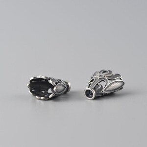 May include: Two silver-toned metal bead caps with an intricate, ornate design. The caps are open at one end and have a closed end with a small hole for threading.