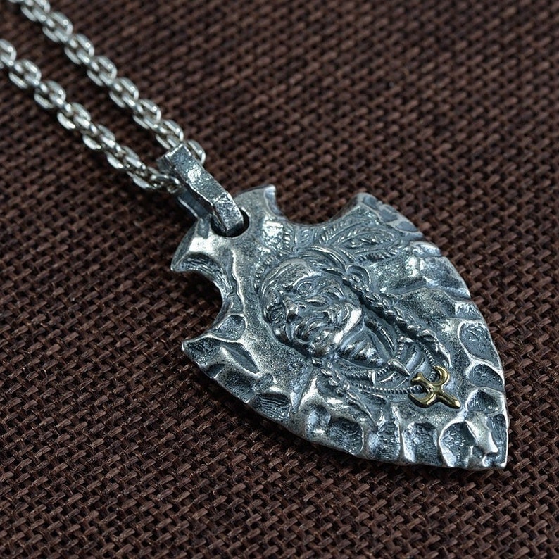 May include: Silver pendant necklace featuring a detailed arrowhead design with a Native American face and a gold accent.