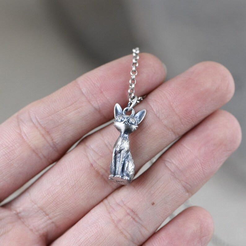 Puede incluir: Un collar de plata con un colgante de gato tridimensional detallado. El gato est&aacute; sentado con las orejas levantadas y tiene un dise&ntilde;o realista.
