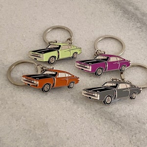 May include: Four keychains featuring different coloured vintage muscle cars. The cars are black with green, purple, orange, and grey paint accents. Each keychain has a silver ring.