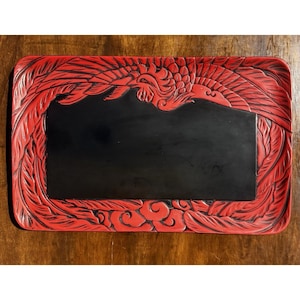 May include: A rectangular red tray with a black center. The tray features a carved phoenix design around the edges. The phoenix is detailed with feathers and a stylized head. The tray is likely made of wood or a similar material.