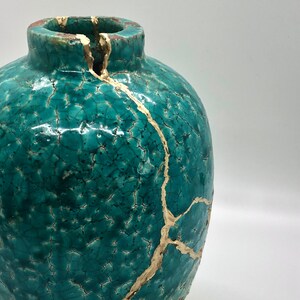 May include: A teal ceramic vase with gold crackle glaze. The vase has a round body and a wide opening.