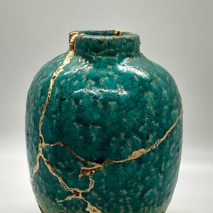 May include: A teal ceramic vase with gold crackle glaze. The vase has a round body and a narrow neck.