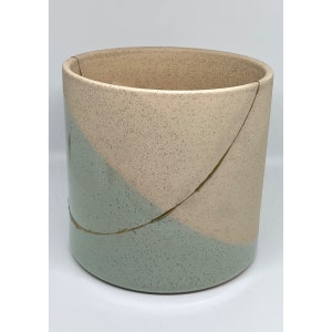 May include: A ceramic planter with a crack running through it. The planter is split into two sections, one light beige and the other light blue.