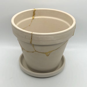 May include: A white ceramic planter with a gold crackle design. The planter has a matching saucer.
