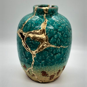 May include: A teal ceramic vase with gold crackle glaze and a crackled finish. The vase has a round body and a narrow neck.
