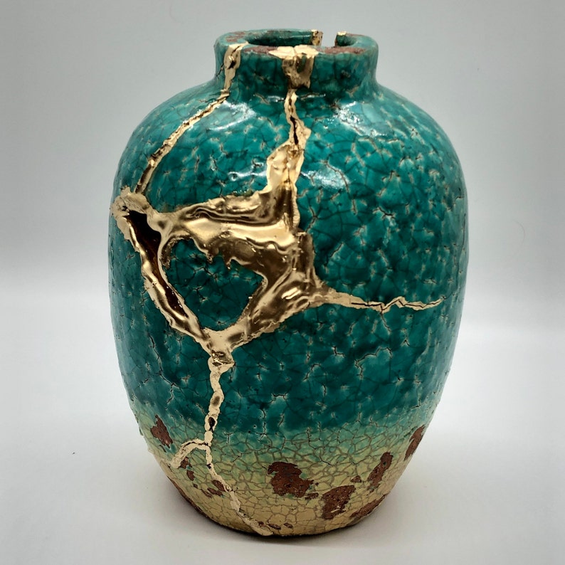 May include: A teal ceramic vase with gold crackle glaze and a crackled finish. The vase has a round body and a narrow neck.