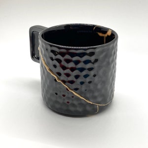 May include: Black ceramic mug with a textured surface and gold crackle design. The mug has a handle and says "Starbucks" on the side.