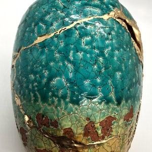 May include: A teal ceramic vase with gold crackle glaze and a rustic brown base. The vase has a unique, distressed look with gold accents.