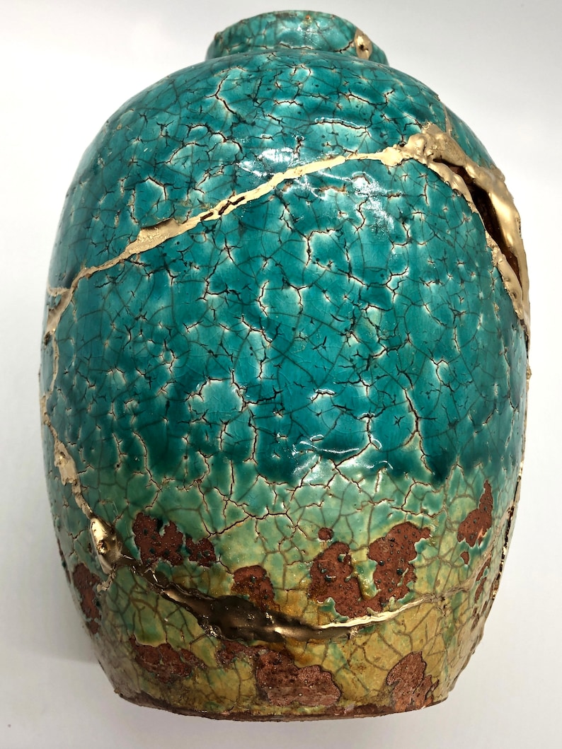 May include: A teal ceramic vase with gold crackle glaze and a rustic brown base. The vase has a unique, distressed look with gold accents.