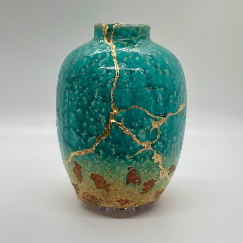 May include: A turquoise ceramic vase with gold crackle glaze and a distressed finish. The vase has a round body and a narrow neck.