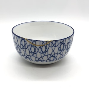 May include: A white ceramic bowl with a blue and gold geometric pattern. The bowl has a crack on the rim.