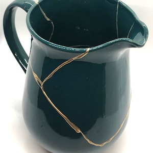 May include: A teal blue ceramic pitcher with gold crackle lines. The pitcher has a wide mouth and a handle.