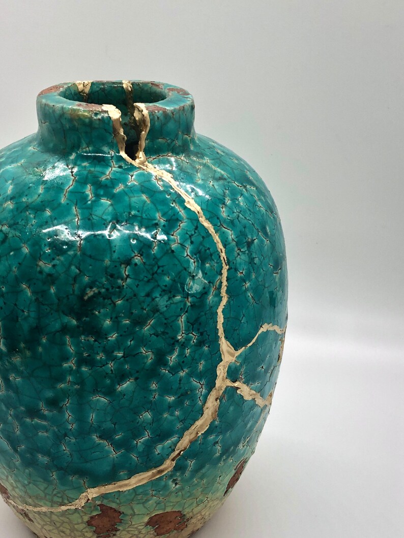 May include: A teal ceramic vase with gold crackle glaze. The vase has a round body and a wide opening.