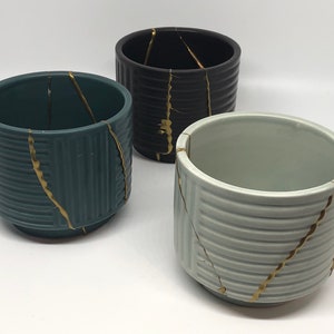 May include: Three ceramic planters with gold crackle details. The planters are in black, teal, and white.
