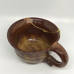 May include: A brown ceramic mug with a gold glaze detail. The mug has a rounded shape and a handle.