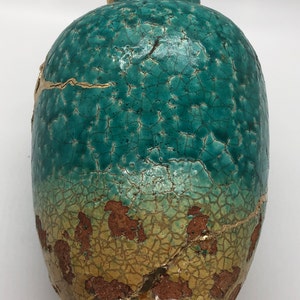 May include: A teal ceramic vase with a crackled glaze and gold accents. The vase has a rounded body and a wide opening.