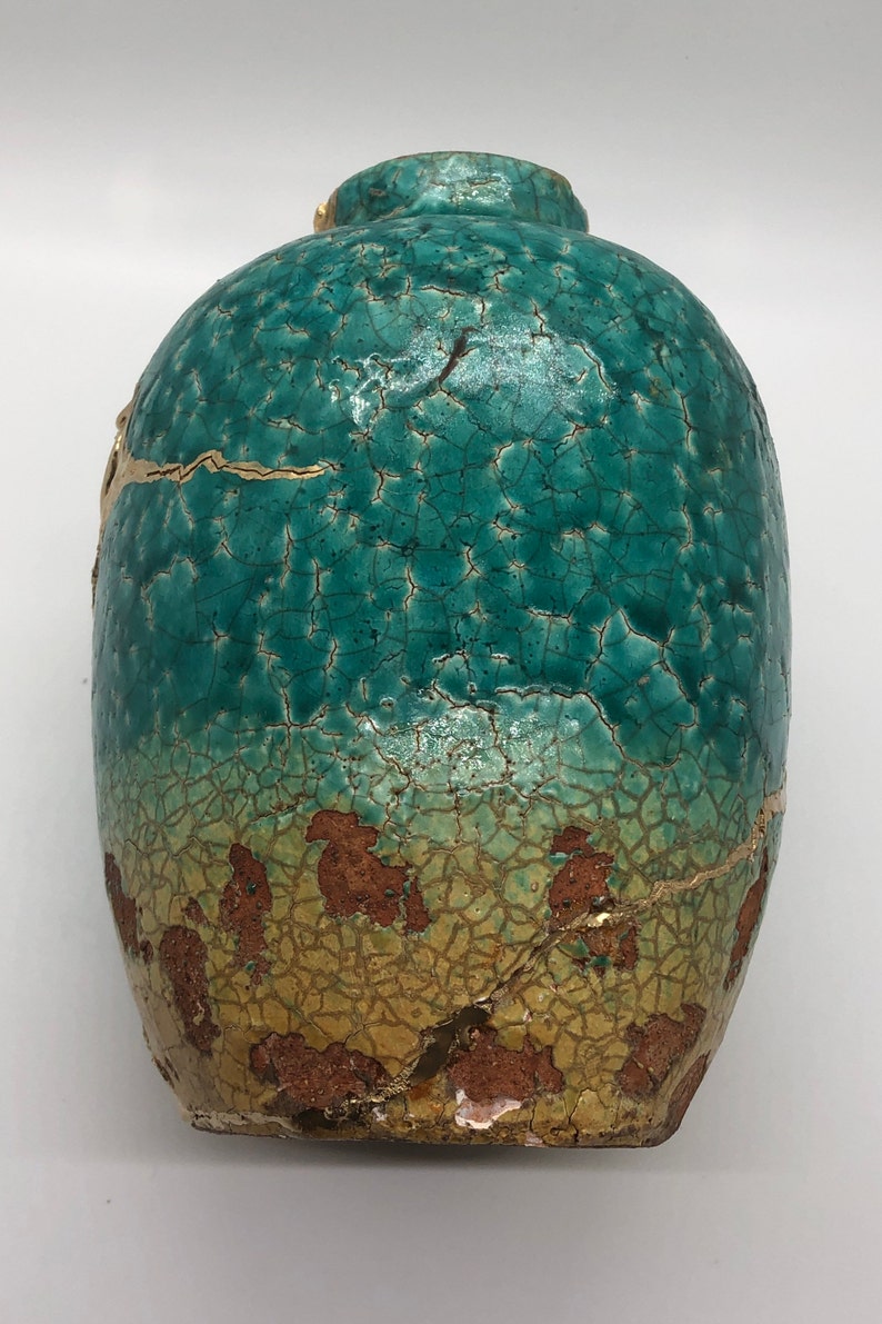 May include: A teal ceramic vase with a crackled glaze and gold accents. The vase has a rounded body and a wide opening.