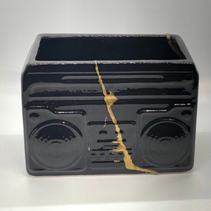 May include: Black ceramic planter shaped like a vintage boombox with gold accents.