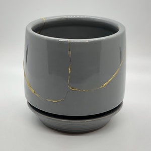 May include: A gray ceramic planter with a gold crackle design. The planter has a matching saucer.