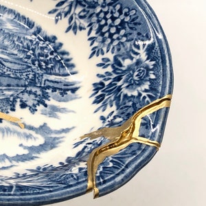 May include: A blue and white porcelain bowl with a floral pattern and gold accents. The bowl is cracked and repaired with gold paint.