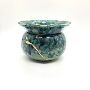 May include: A green and blue ceramic planter with a gold crackle glaze. The planter has a wide, scalloped rim and a round body.