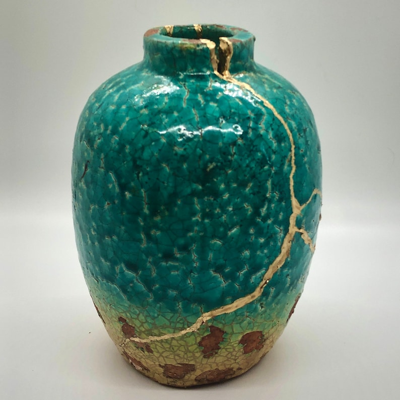 May include: A teal blue ceramic vase with gold crackle glaze and gold accents. The vase has a round body and a narrow neck.