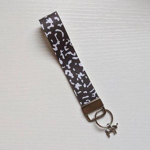 May include: A brown and white patterned key chain with a silver key ring and a silver cow charm.